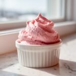 A perfectly piped swirl of light pink Raspberry Mousse served in a white fluted ramekin.