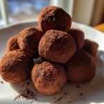 A stack of homemade Raspberry Truffles generously dusted with dark cocoa powder on a white plate.