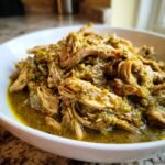 Close-up of tender, shredded pork loin covered in vibrant green chile verde sauce in a white bowl.