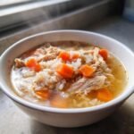Close-up of a steaming white bowl filled with Souper Rice, shredded chicken, and bright orange diced carrots in broth.