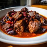 Close-up of a rich, deep red bowl of Texas Cowboy Stew featuring large chunks of beef and kidney beans.