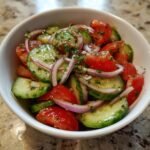 Close-up of a refreshing Tomato Cucumber Salad with sliced red onions and herbs in a white bowl.