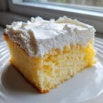 Close-up of a moist slice of Tres Leches Cake With Cake Mix topped with fluffy white whipped cream.