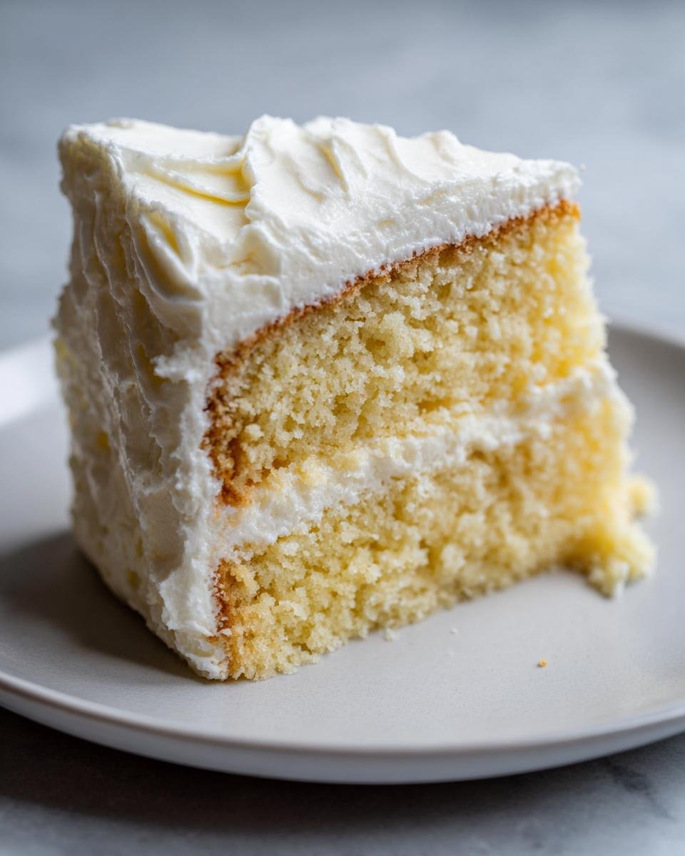 Close-up of a moist slice of vanilla layer cake with thick white frosting, perfect for Mothers Day Cakes.