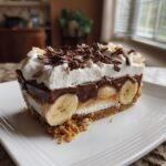 A decadent slice of Banoffee Pie featuring layers of crust, banana, chocolate pudding, and whipped cream topped with chocolate shavings.