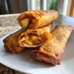 Close-up of crispy, golden Apple Pie Egg Rolls, one cut open to show the spiced apple filling.