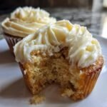 Close-up of a White Chocolate Cupcakes with a bite taken out, showing the moist crumb and thick white chocolate frosting.