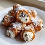 A pile of freshly made Cannoli Bites dusted with powdered sugar and garnished with mini chocolate chips.