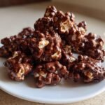 A mound of freshly made Chocolate Covered Popcorn clusters piled high on a white plate.