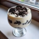 A serving of creamy Oreo Pudding layered with crushed chocolate cookies, topped with whole and crumbled Oreos.