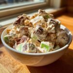 A close-up, brightly lit bowl filled with creamy Snickers Salad, featuring chunks of chocolate, caramel, and green apple pieces.