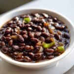 Close-up of a white bowl filled with rich, dark Cuban Black Beans cooked with onions and green peppers.