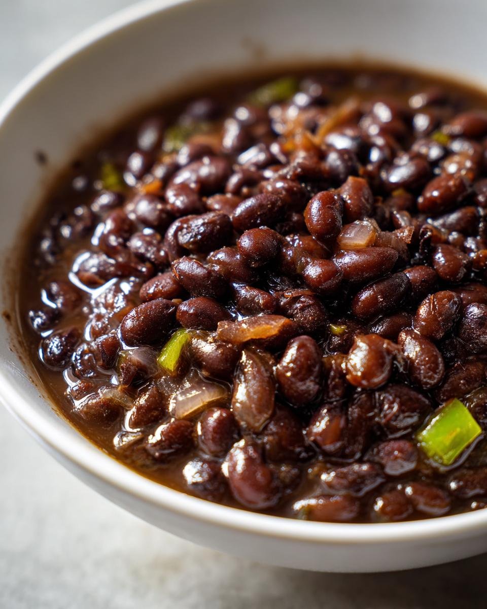 Close-up of rich, saucy Cuban Black Beans cooked with onions and green peppers in a white bowl.