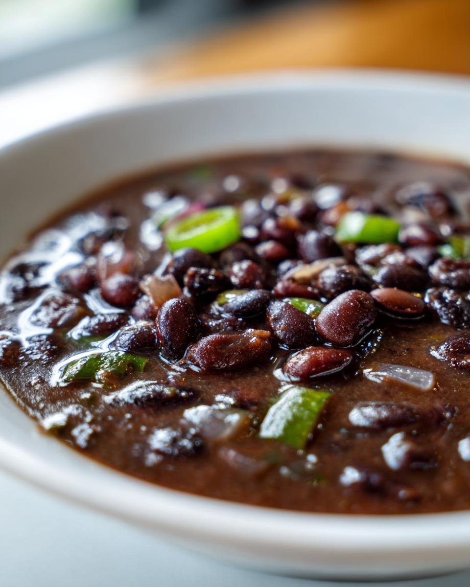 A close-up, appetizing shot of rich, dark Cuban Black Beans stewed with onions and topped with bright green pepper slices.