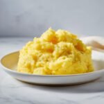 A mound of bright yellow, fluffy Mashed Rutabaga seasoned with black pepper, served in a white bowl.