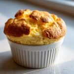 A perfectly risen, golden-brown Sweet Potato Souffle baked in a white, ribbed ramekin.