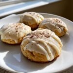 Four delicious Frosted Eggnog Cookies drizzled with glaze and sprinkled with nutmeg on a white plate.