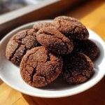 A close-up of several dark, crinkled Gingersnap Cookies coated in sparkling sugar on a white plate.