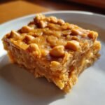 A single, thick square of rich, gooey Butterscotch Bars topped with melted butterscotch chips, resting on a white plate.