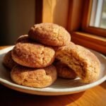 A stack of soft, thick Maple Snickerdoodles coated in cinnamon sugar, one cookie is broken open showing the chewy interior.