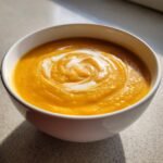 Close-up of a bowl of vibrant orange Panera Autumn Squash Soup, swirled with cream.