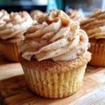 A close-up shot of a freshly baked Snickerdoodle Cupcakes topped with swirled cinnamon frosting and sprinkled with cinnamon sugar.