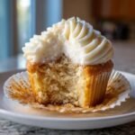 Close-up of a White Chocolate Cupcakes with a bite taken out, showing moist cake and thick white frosting.