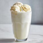 A tall glass filled with frothy White Christmas Punch, topped with three generous scoops of vanilla ice cream.