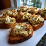 Close-up of several pieces of Artichoke Bruschetta with melted, browned cheese topping served on toasted baguette slices.