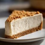 A perfect slice of The Best No Bake Cheesecake showing a thick, creamy filling and graham cracker crust, topped with crumbs.