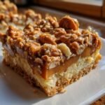 A close-up, sunlit view of a single square of Butterfinger Caramel Bars showing the crust, caramel layer, and peanut topping.