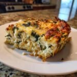 A close-up of a cheesy, baked slice of Chicken Tortilla Spinach Casserole with shredded chicken and spinach.