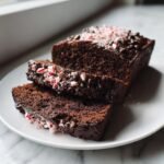 Close-up of sliced Chocolate Peppermint Bread topped with crushed candy canes and chocolate chips on a white plate.