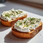 Two slices of toasted bread topped generously with creamy Cottage Cheese Breakfast Toast, herbs, and pepper.