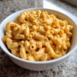 Close-up of a white bowl filled with creamy, bright orange Mac And Cheese made with elbow macaroni.
