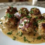 Close-up of browned Creamy Mushroom Chicken Meatballs covered in a rich, light brown sauce and garnished with fresh parsley.