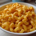 Close-up of rich, creamy, orange cheese sauce coating elbow macaroni in a white bowl of Mac And Cheese.