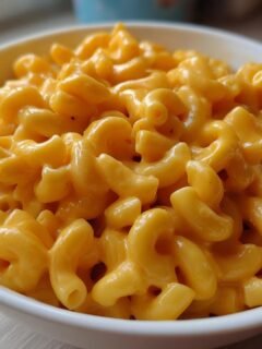 Close-up of rich, creamy, orange cheese sauce coating elbow macaroni in a white bowl of Mac And Cheese.