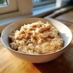 A close-up of a bowl filled with creamy Crock Pot Chicken And Rice, topped with shredded chicken.