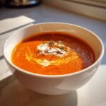 A vibrant bowl of Exquisite Lobster Bisque With Saffron Infusion, garnished with cream swirl and saffron threads.