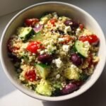A close-up overhead view of a Mediterranean Quinoa Power Bowl featuring quinoa, cucumbers, tomatoes, olives, and feta cheese.