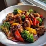 A close-up of One Pan Balsamic Chicken And Veggies featuring glazed chicken pieces, bright broccoli, red and yellow peppers, and onions in a white bowl.