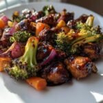 Close-up of One Pan Balsamic Chicken And Veggies, featuring glazed chicken pieces, broccoli, carrots, and red onion.