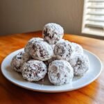 A pile of rich Puppy Chow Chocolate Truffles heavily coated in white powdered sugar, served on a white plate.