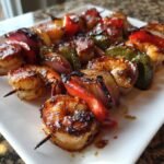 Close-up of perfectly grilled Sausage Grilled Shrimp Kabobs with charred shrimp, red onion, and bell peppers on a white plate.