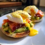 Close-up of Smoked Salmon And Avocado Eggs Royale with runny yolk dripping onto a white plate.